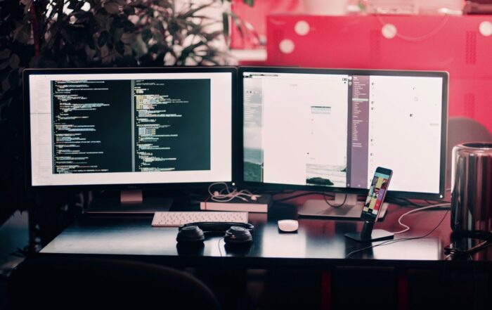 Two Black Computer Monitors on Black Table 3rd line support